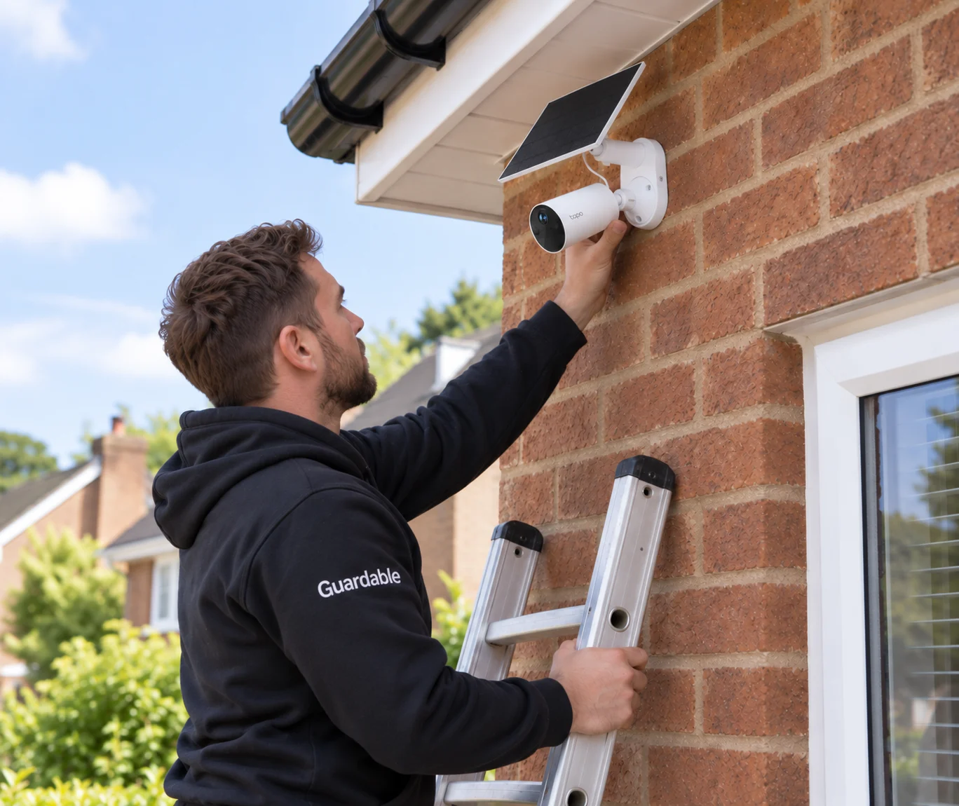 Guardable installer fitting a Tapo solar security camera high on a brick home